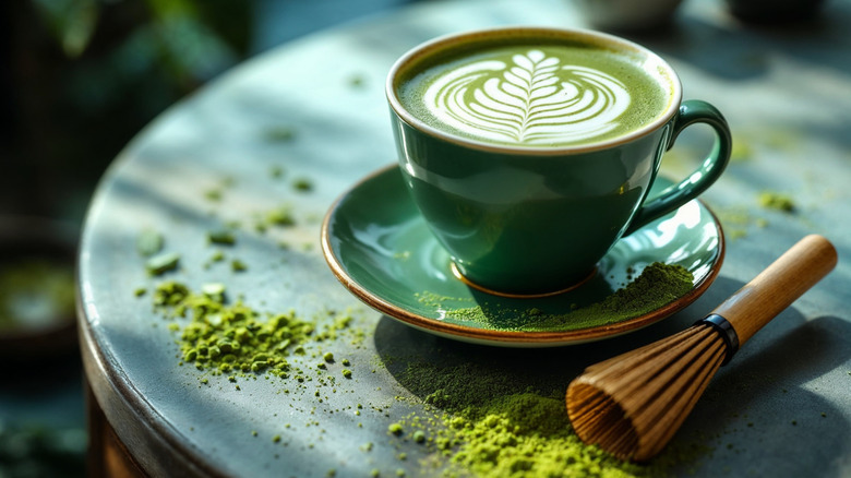 A hot matcha latte on a table with a matcha whisk and matcha powder on the table