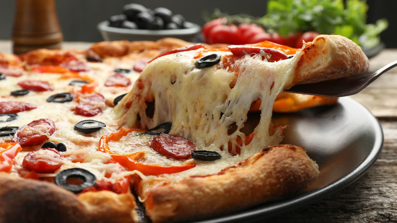A slice of pizza is lifted from a round metal tray using a spatula
