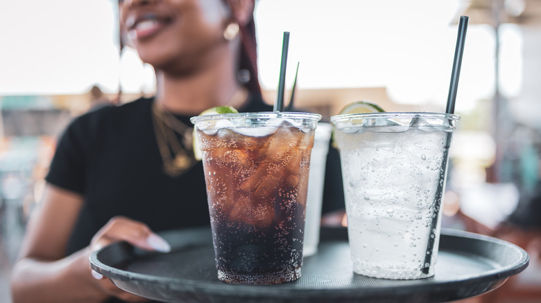 A server holds sodas on a tray