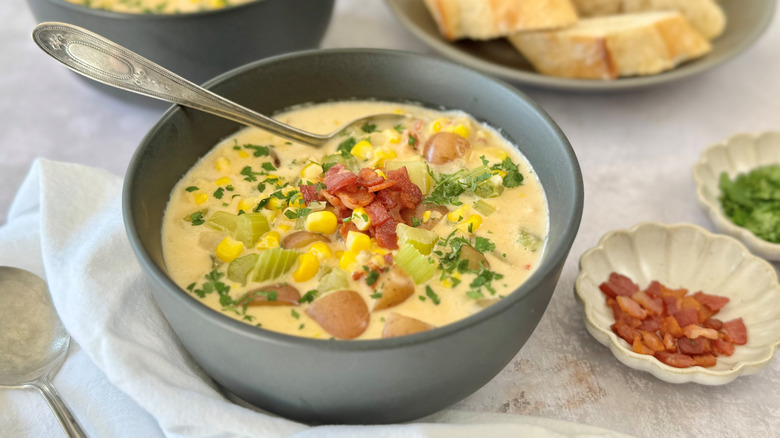 Corn chowder in bowl topped with bacon and herbs