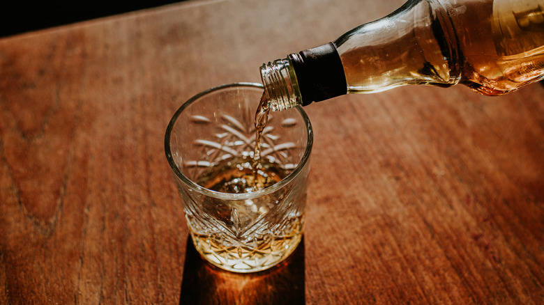 A bottle of whisky poured into a cut glass.