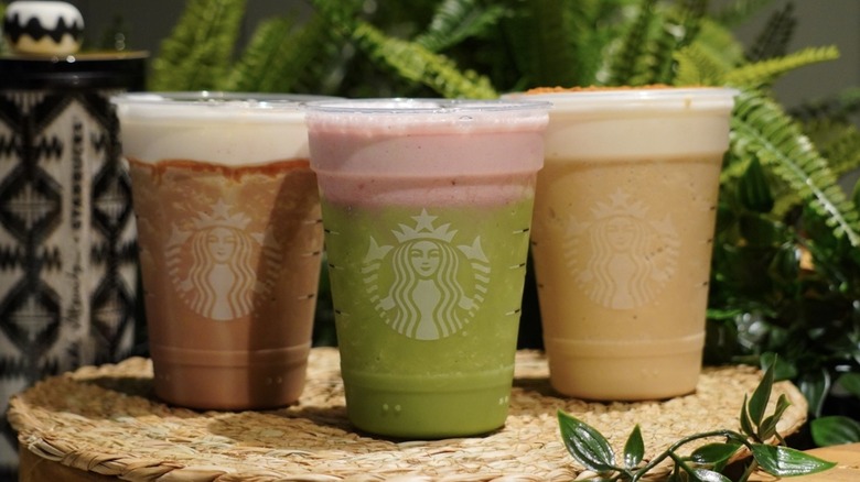 Starbucks' Salted Caramel Mocha Strato Frappuccino, Strawberry Matcha Strato Frappuccino, and Brown Sugar Strato Frappuccino placed on a woven placemat in front of greenery