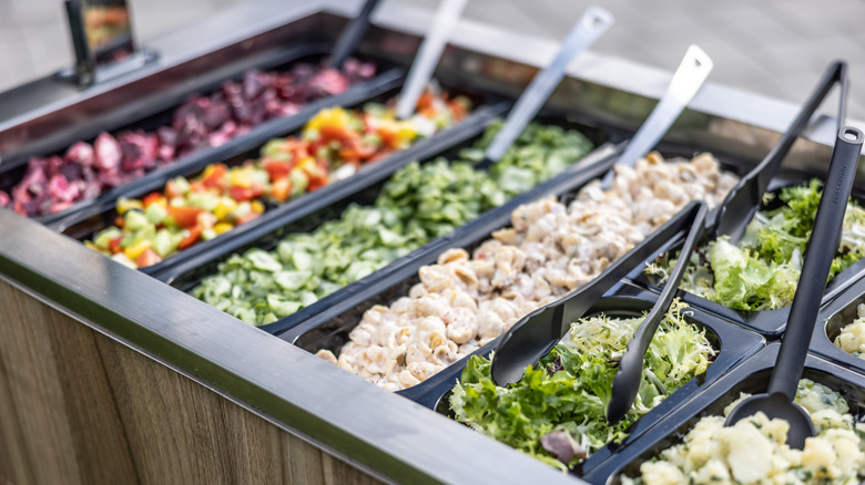 Buffet style salad bar with various lettuces and toppings