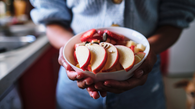 Hands holding sliced apples in bowl