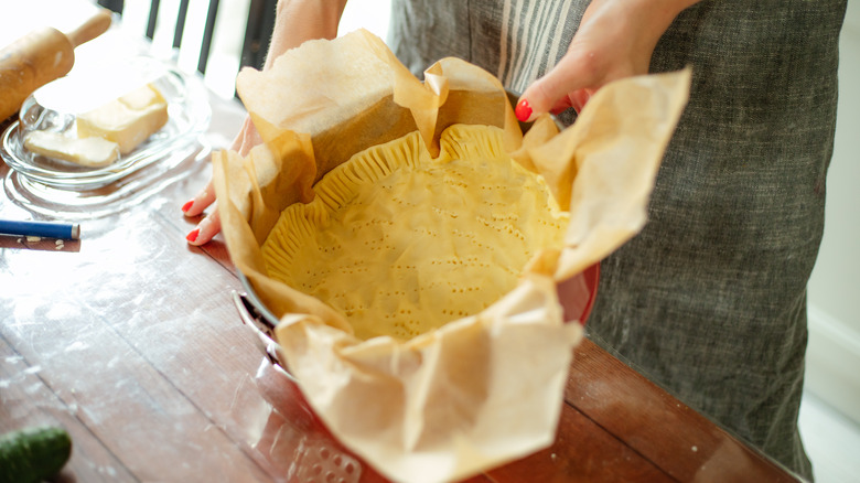 A person holds a pie plate with pie dough in one hand