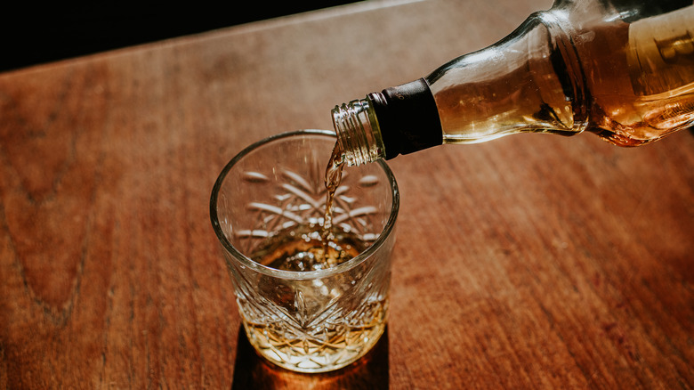 A bottle of whiskey pouring into a glass with ice