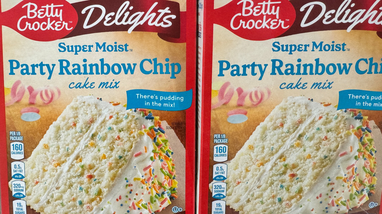 A chocolate cake mix sits in a glass bowl with a wooden spoon, against a wooden background