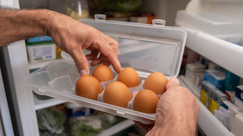 A home cook holds a carton of eggs outside a fridge