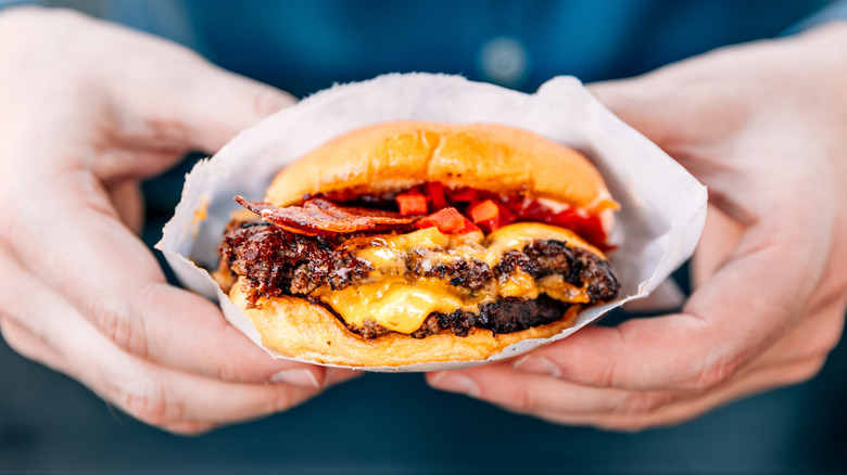 Two hands hold onto a cheeseburger in a paper sleeve