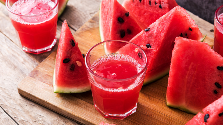 A glass of fresh watermelon juice next to slices of red watermelon.