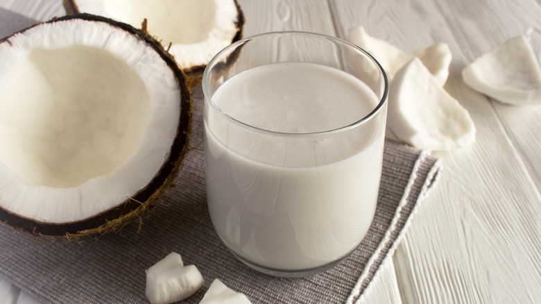 A glass of coconut milk and a halved coconut
