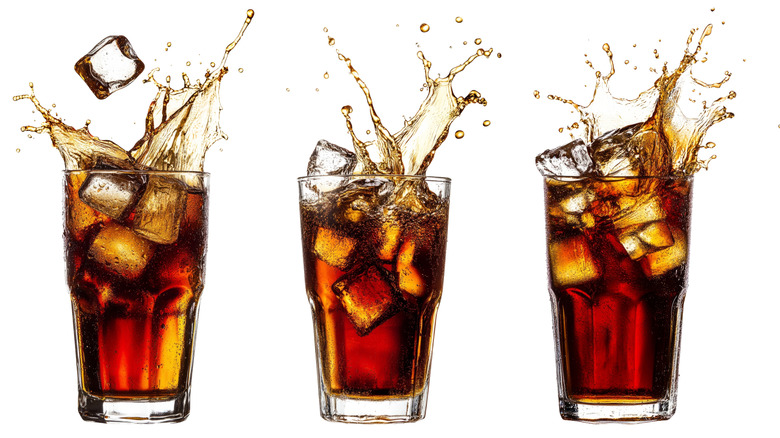 Three glasses of soda have ice falling into them