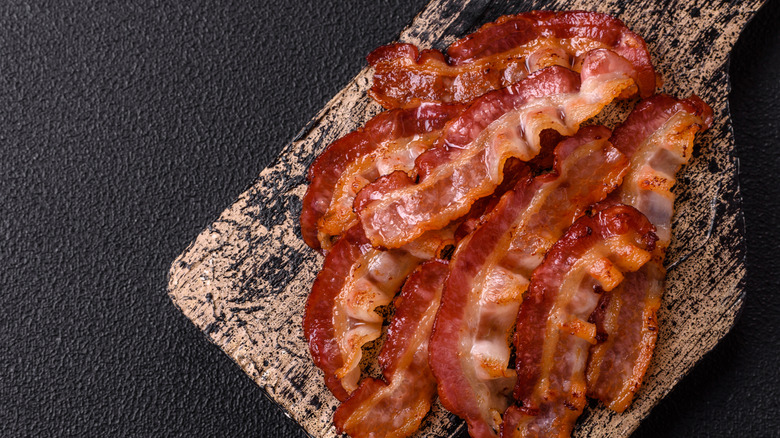 Bacon on a cutting board on a dark background.