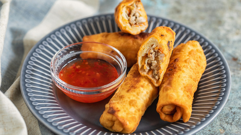 Egg rolls sit on a plate with dipping sauce in a bowl
