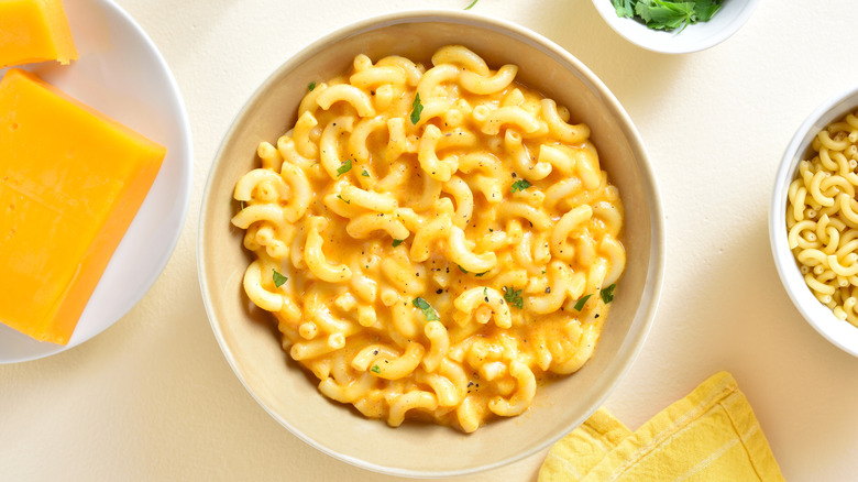 Creamy mac and cheese sits in a white bowl, with ingredients around it