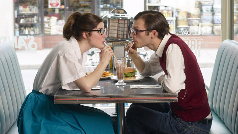 Retro-looking couple sharing a chocolate drink in the booth of an old-time looking diner