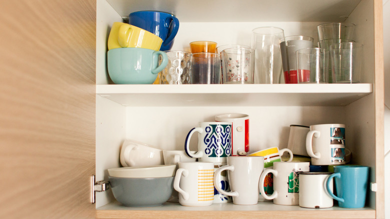 Open cupboard with mugs, glasses, and bowls stacked inside.