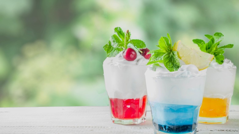 Three Italian cream sodas sit on a white surface against a blue-green background