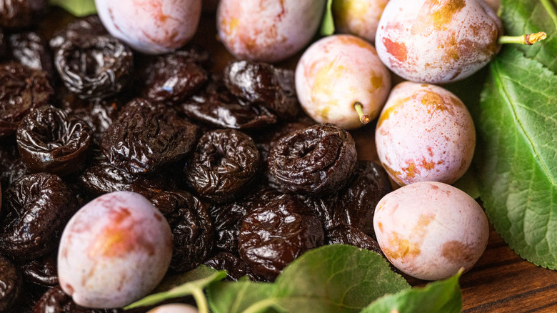 Prunes on a wooden board surrounded by plums and leaves