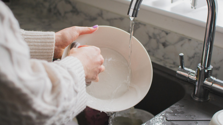 Close up of a person washing a dish under a running faucet