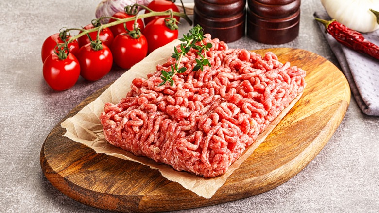 Fresh ground beef on parchment sitting on a wooden board, tomatoes surrounding it