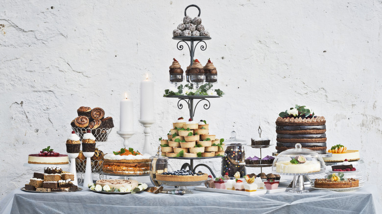 A table with a gray tablecloth is covered in myriad desserts, from cheesecake and cupcakes to tarts, rolls, and petit fours