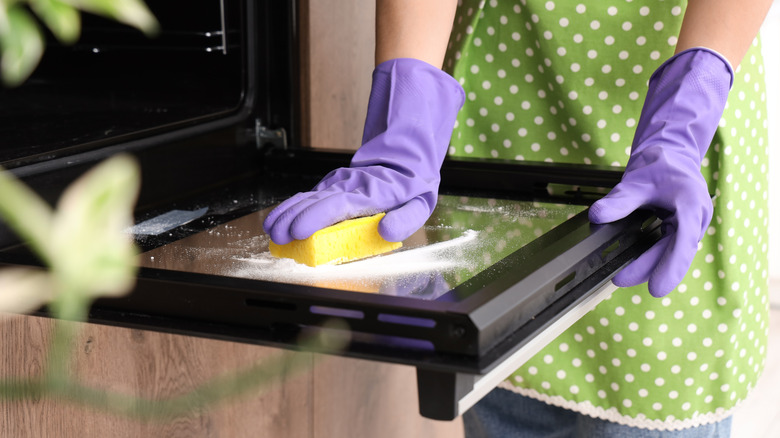 Person cleaning oven door with sponge