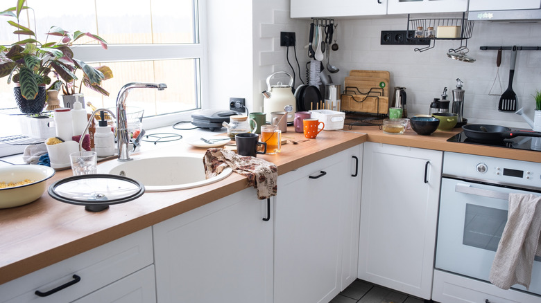 A cluttered kitchen with dirty dishes and various items spread across the counter
