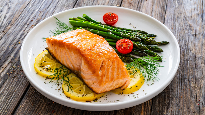 cooked salmon on a plate with lemon, asparagus, and tomatoes