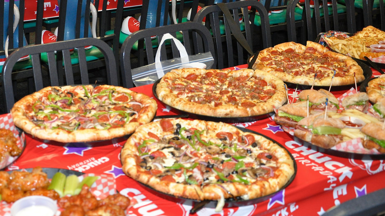 Multiple pizzas sit on a long table with a Chuck E. Cheese-branded tablecloth