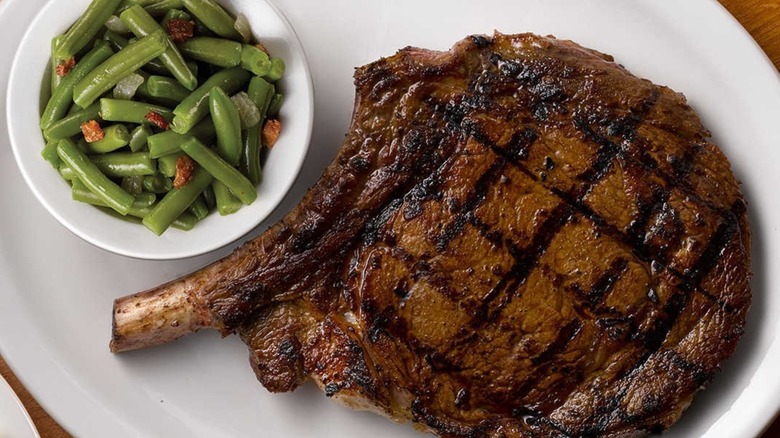 Bone in rib eye and a side of green beans on a white plate