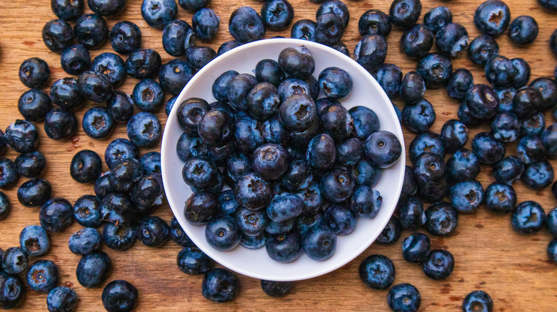Blueberries in a white bowl and scattered across tabletop