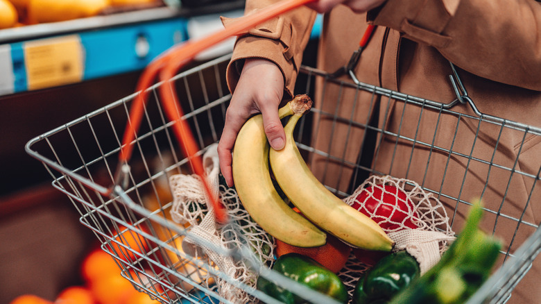 A person puts a bunch of yellow bananas in a shopping basket.