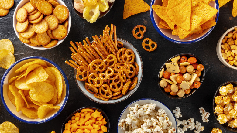 Various snack foods sit in separate bowls, including pretzels, tortilla chips, crackers, and popcorn