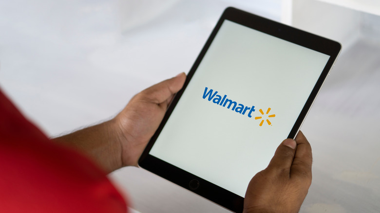 A man holds a tablet with the Walmart app logo