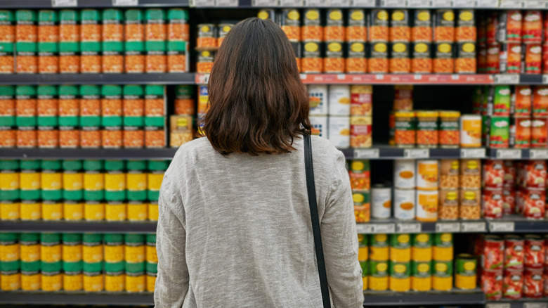 a shopper stands before a wall of canned baked beans in a grocery store