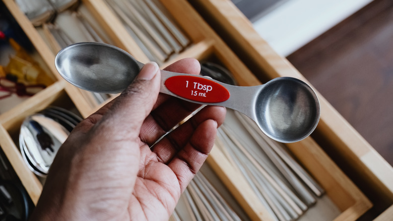 A woman getting a measuring spoon from the drawer that has an oval side and a round side