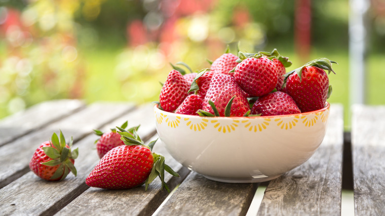 A pretty bowl of strawberries sits on a wooden surface outside