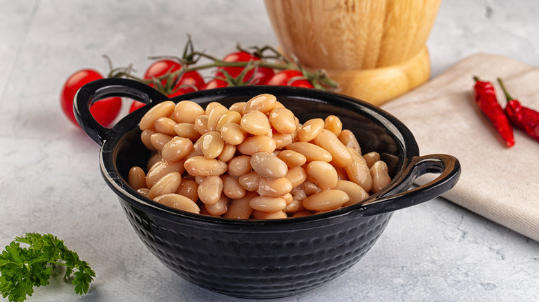 canned white beans sit in a black bowl next to fresh parsley, tomatoes, and dried chilis