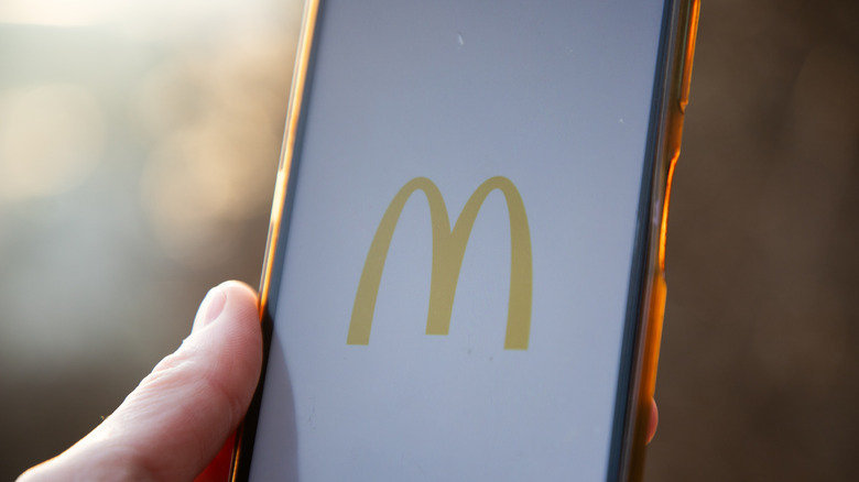 A hand holds a cell phone with the McDonald's app logo on the screen
