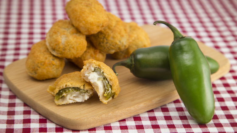 A wooden cutting board full of jalapeno poppers on a red gingham check tablecloth