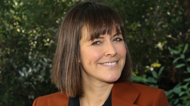 Leanne Ford smiling in a burnt orange blazer with foliage background.