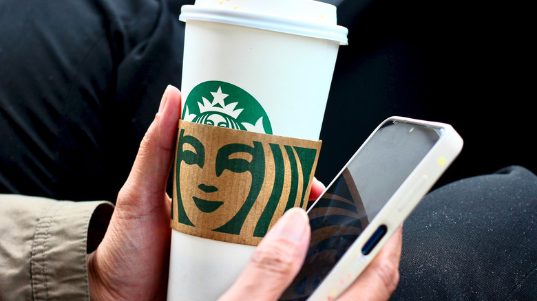 Someone holding a Starbucks cup and a phone