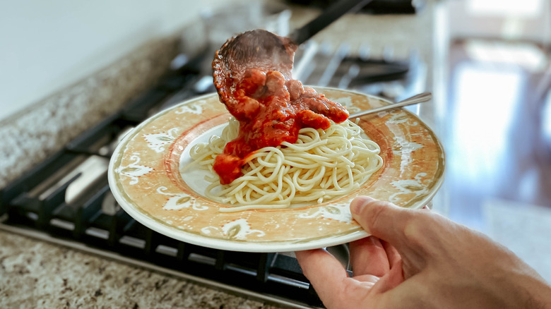 A man spooning some marinara sauce on to his dish