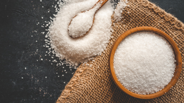 Bowl of table salt with mound of salt and spoon next to it.