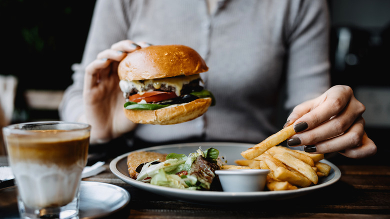 A woman holds a burger in one hand and a fry in the other