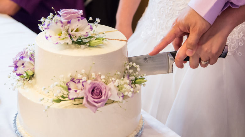 A bride and groom cut into a wedding cake that is adorned with edible flowers