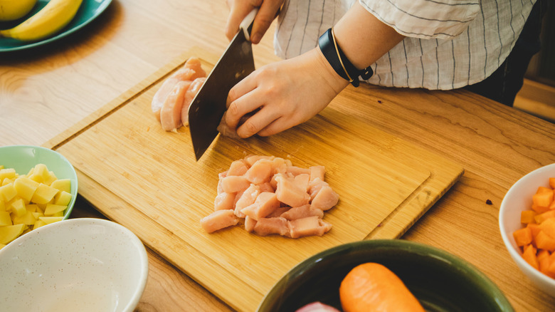Person cutting chicken on wooden cutting board