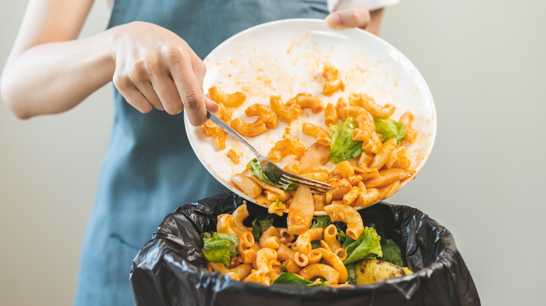 Person throwing away leftover pasta