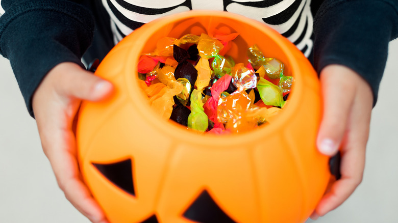 A pumpkin trick-or-treat container contains lots of candy